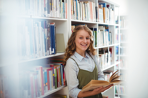 Portrait of happy schoolgirl reading book in library at school