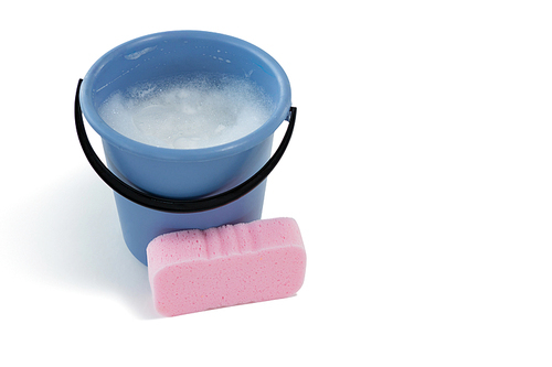Sponge by bucket containing soap sud against white background