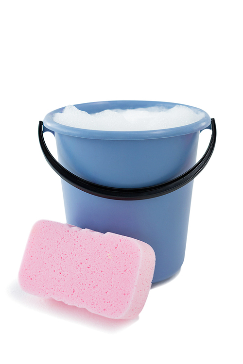 Close up of sponge by bucket containing soap sud against white background