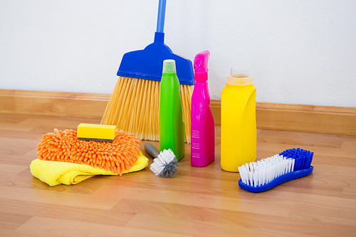 Chemical bottles by brush and sponges with broom on floor against wall
