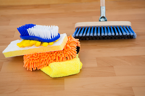 Close-up of sponges and brush by broom on hardwood floor