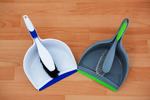 Overhead view of colorful brushs with dustpans on hardwood floor