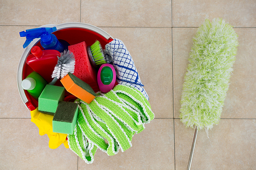 Overhead view of duster by various cleaning products in bucket on tiled floor