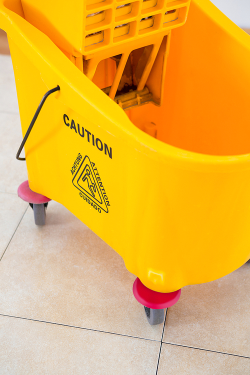Close up of yellow mop bucket on tiled floor