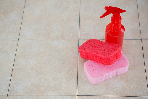 High angle view of cleaning sponge with spray bottle on tiled floor