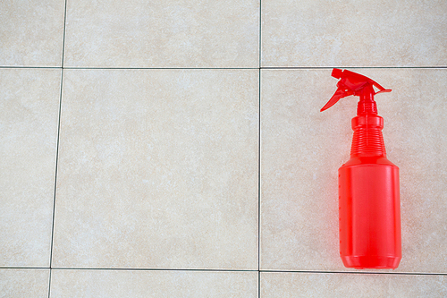Overhead view of red spray bottle on tiled floor