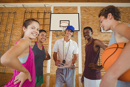 Portrait of smiling of smiling high school kids and their coach standing in the basketball court