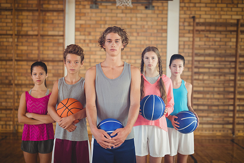Portrait of confident high school kids holding basketball in the court