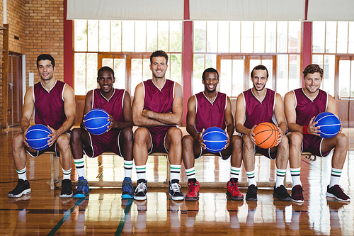 Portrait of smiling basketball players sitting on bench with basketball in the court