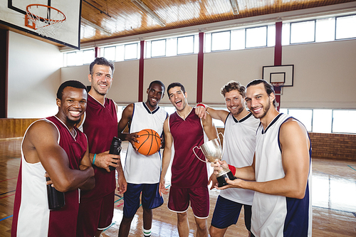 Portrait of smiling basketball players standing with throphy in the court