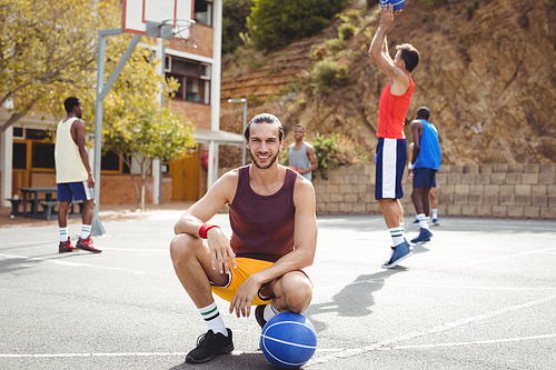 Portrait of basketball player with basketball sitting in basketball court