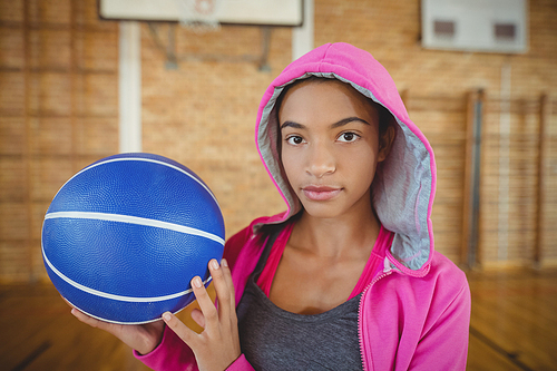 Determined high school girl standing with basketball in the court