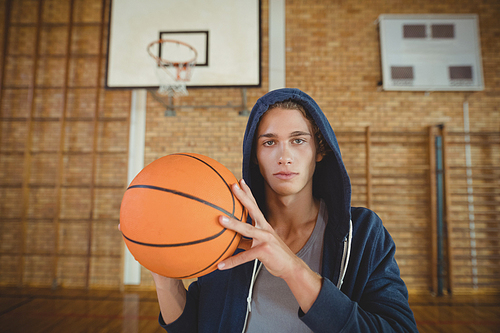Determined high school boy standing with basketball in the court