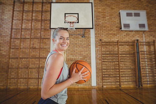 Happy high school girl standing with basketball in the court