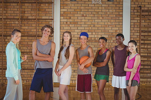 Portrait of female coach and high school kids standing in basketball court