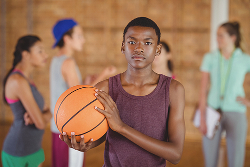 Determined high school boy standing with basketball in the court