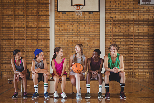High school kids sitting on a bench in basketball court indoors
