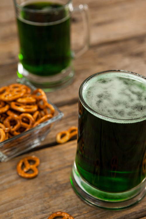 St Patricks Day two mugs of green beer with pretzel on wooden surface