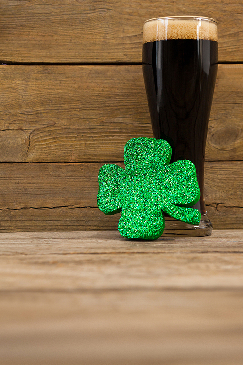 Glass of black beer and shamrock for St Patricks Day against wooden background