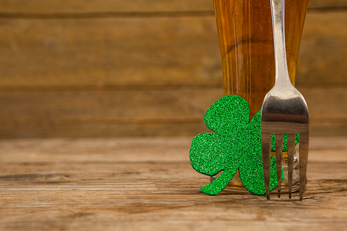 Glass of beer, fork and shamrock for St Patricks Day against wooden background