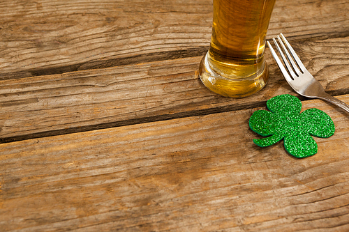 Glass of beer, fork and shamrock for St Patricks Day against wooden background