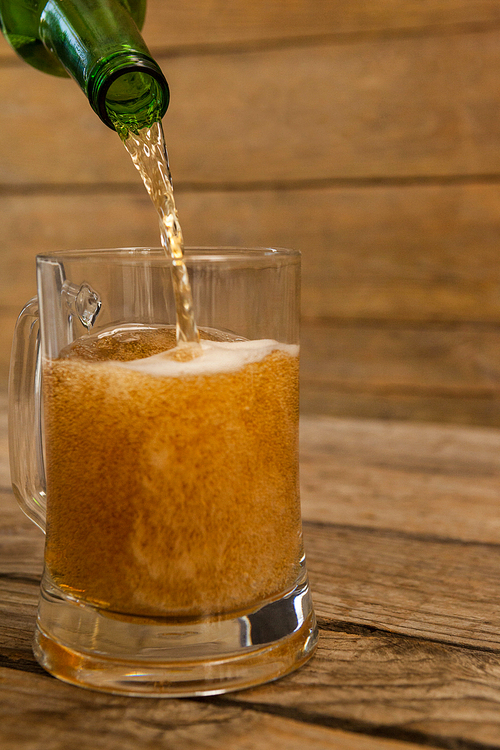 Beer being poured into a mug against wooden background