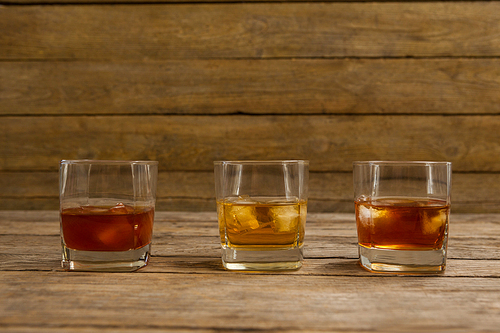 Three glasses of whiskey with ice cube on wooden table