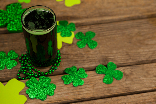 Glass of green beer, beads and shamrock for St Patricks Day on wooden table