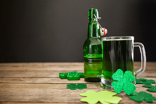 Mug of green beer, beer bottle and shamrocks for St Patricks Day on wooden table