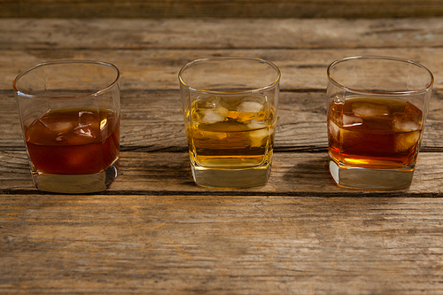 Three glasses of whiskey with ice cube on wooden table