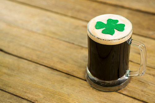 St Patricks Day mug of beer with shamrock on wooden surface