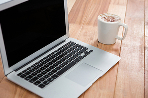 Mug of coffee and laptop on wooden background