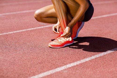 Low section of female athlete tying shoelace on track