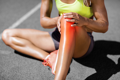 Low section of sportswoman suffering from joint pain while sitting on track during sunny day