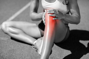 Low section of female athlete suffering from joint pain while sitting on track during sunny day