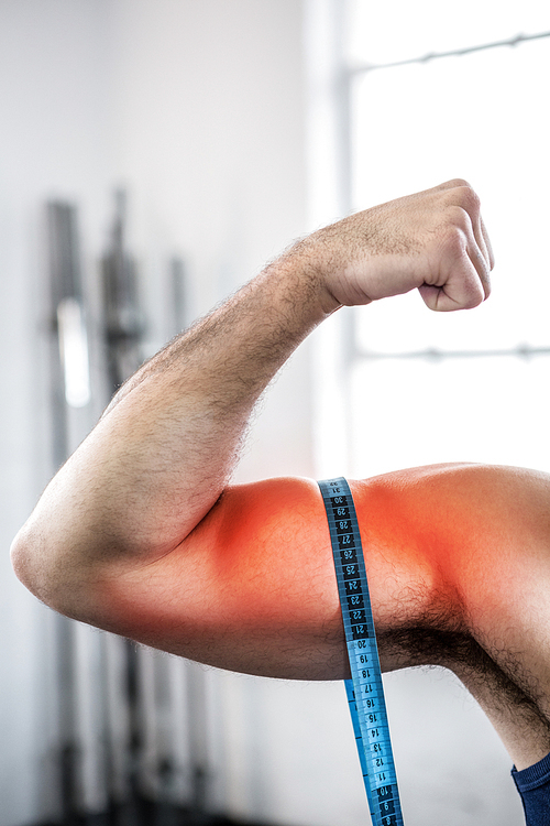 Digital composite of highlighted arm of man measuring biceps with measuring tape