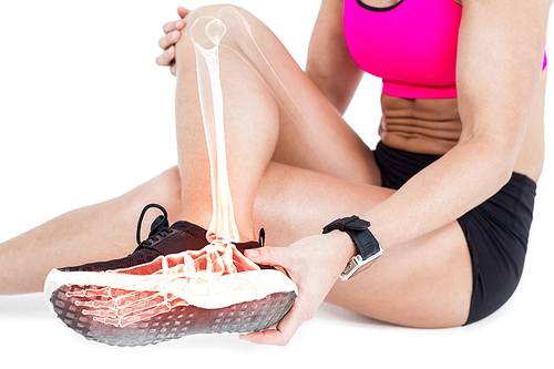 Low section of woman suffering from ankle pain while sitting on white background