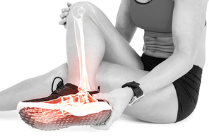 Low section of female athlete suffering from ankle pain while sitting on white background