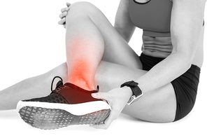 Low section of female sportsperson suffering from ankle pain while sitting on white background