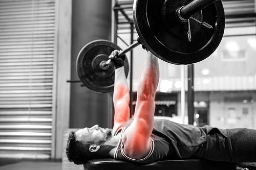 Side view of male athlete exercising with barbell at gym