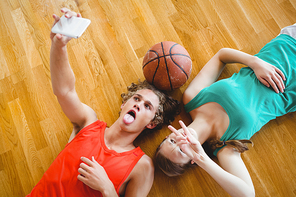 Overhead view of friends taking selfie while lying on hardwood floor in court