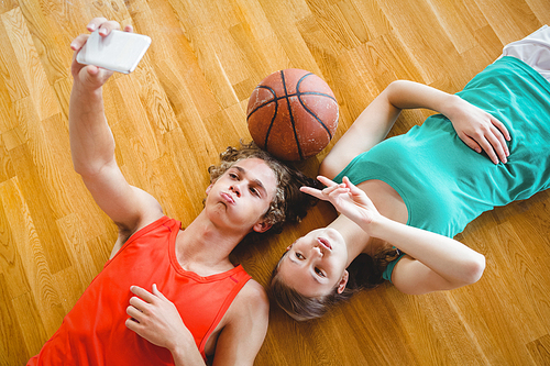 Overhead view of playful friends taking selfie while lying on hardwood floor in court