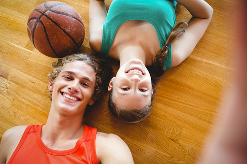 Overhead portrait of smiling friends lying on floor in basketball court