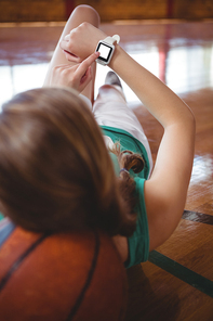 Female basketball player using smart watch while relaxing in court