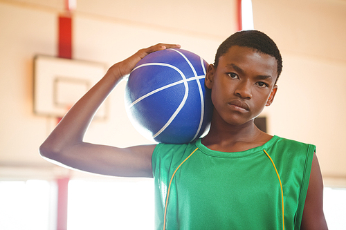 Portrait of confident teenage boy holding basketball while standing in court