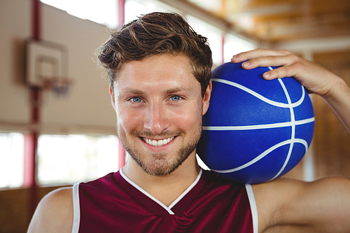 Close up portrait of smiling basketball player holding ball while standing in court