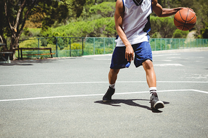 Low section of male teenager practicing basketball at court on sunny day