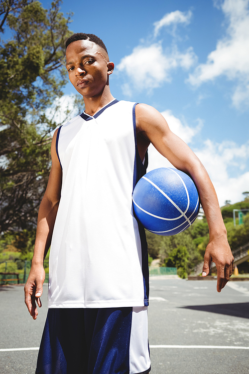 Portrait of male teenager holding ball while standing in court on sunny day