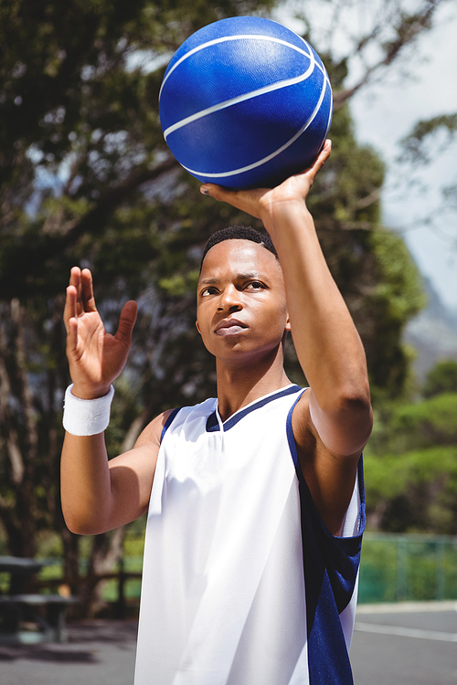 Teenage boy holding basketball while practicing in court on sunny day