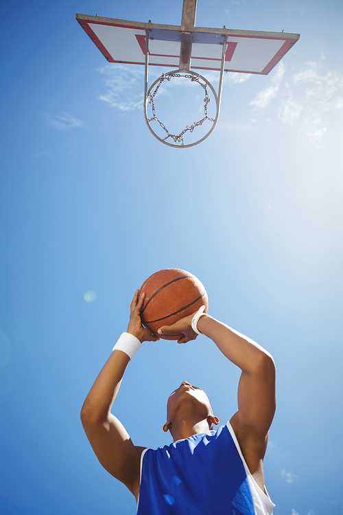 Directly below shot of teenage boy playing basketball against sky on sunny day